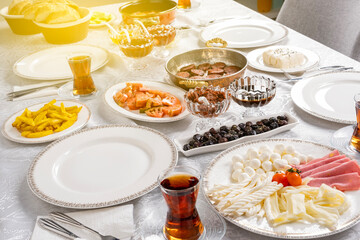 Modern breakfast table at home, ready for friends or family. Morning sun light. Delicious start for the day. Sunday Turkish routine. Tea in glass, sucuk in frying pan, fried potatoes, cheese plate.
