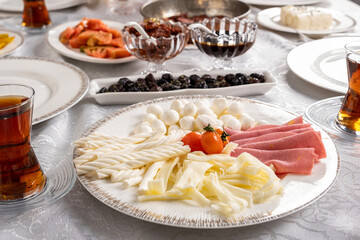Cheese plate, close up photo of string, knit, little round cheese plate. Ham and tomatoes. Hot fresh Turkish tea. Black olive, jam, frying pan blurred background. Traditional breakfast table.