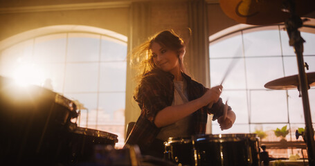 Fototapeta na wymiar Portrait of a Young Female Playing Drums During a Band Rehearsal in a Loft Studio with Warm Sunlight at Daytime. Drummer Girl Practising Before a Live Concert on Stage in Local Venue.