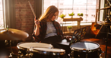 Fototapeta na wymiar Young Musician Taking a Breather, Resting Between Intense Drum Solos. Alternative Stylish Female Using Laptop Computer, Checking Social Media, Chatting with Friends. Loft Living Room on a Sunny Day.