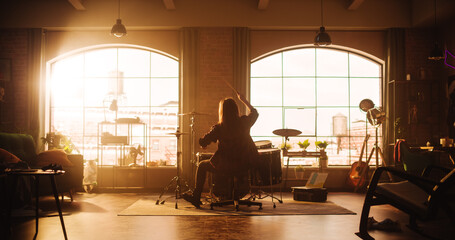 Person Sitting with Their Back to Camera, Playing Drums During a Band Rehearsal in a Loft Studio with Sunlight. Drummer Practising Alone Before a Concert on Stage. Warm Color Editing.