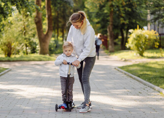 A boy with his mother riding in the park on a scooter