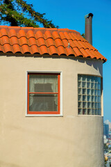 Round turret or spire style exterior wall with visible bay windows and a thin adobe orange roof with tiles and chimney vent