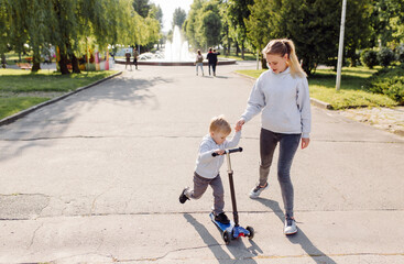 A boy with his mother riding in the park on a scooter