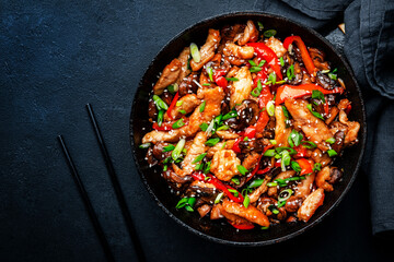 Obraz na płótnie Canvas Stir fry with turkey fillet, paprika, mushrooms, green chives and sesame seeds in frying pan. Asian cuisine dish. Black stone kitchen table background, top view