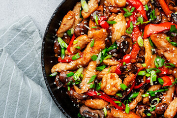 Stir fry with chicken, red paprika, mushrooms and chives in frying pan. Asian cuisine dish. Gray kitchen table background, top view, copy space