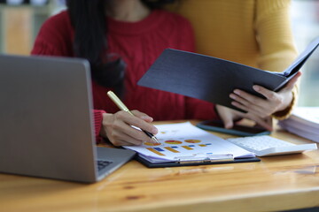 Colleagues work at their office desks together checking documents. Accountants discuss budget accounting and financial planning.