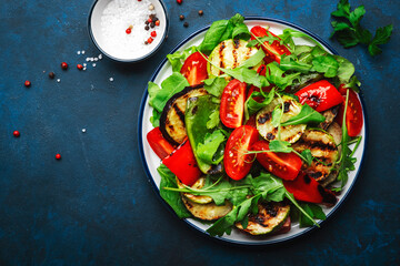 Healthy salad with grilled vegetables, paprika, zucchini, eggplant with fresh tomatoes and mixed herbs. Blue table background, top view