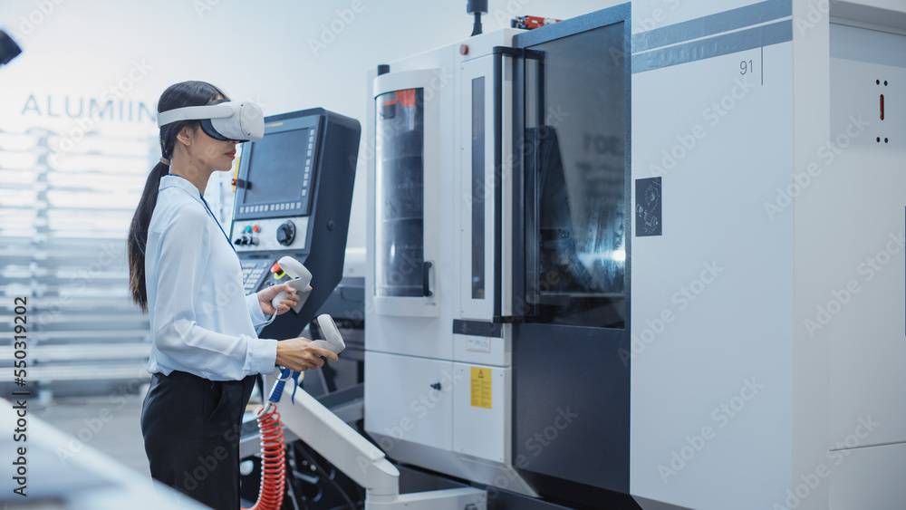 Fototapete Female Engineer Wearing a Virtual Reality Headset and Operating a Heavy Industry Machine with Controllers at a Factory. Technician Configuring Industrial Machinery with the Help of VR Technology.