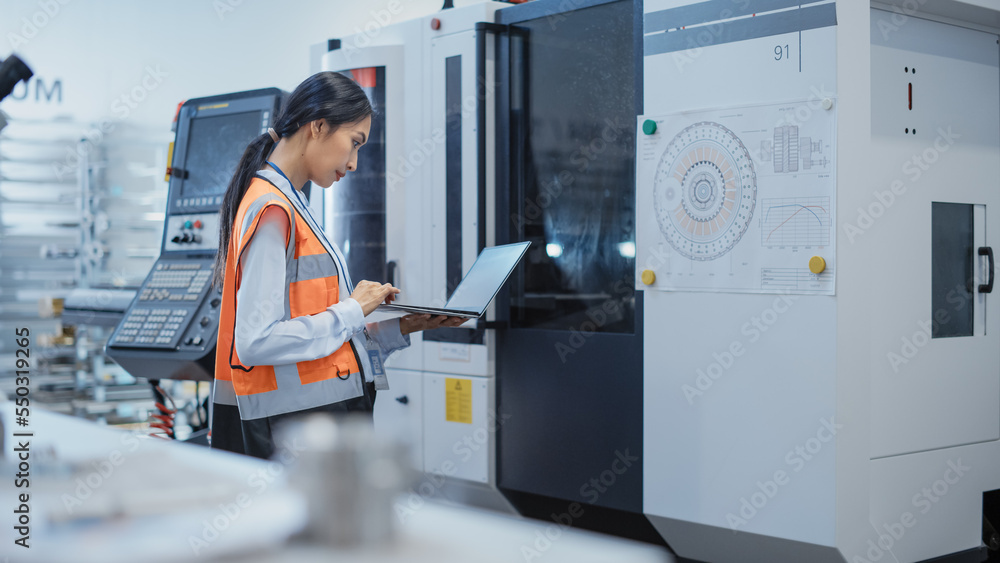 Poster research and development specialist with a laptop comes up to operate a heavy industry machine at a 