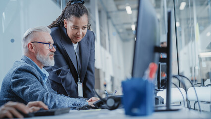 Fototapeta premium Factory Office Facility: Industrial Engineers Drafting Blueprints of a Heavy Industry Machine Parts on a Computer CAD Software. African American Technician Discusses Work with Middle Aged Designer.