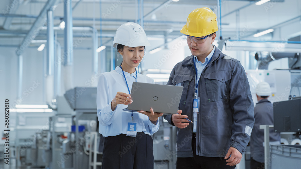 Poster portrait of two young asian heavy industry engineers in hard hats standing with laptop computer and 