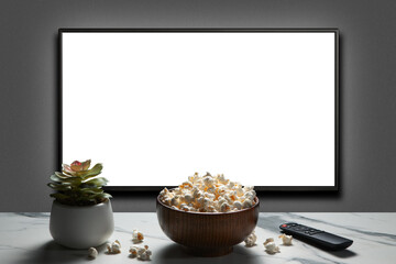 Television on a gray wall with remote control, home plant and popcorn bowl on the table. TV 4K flat...