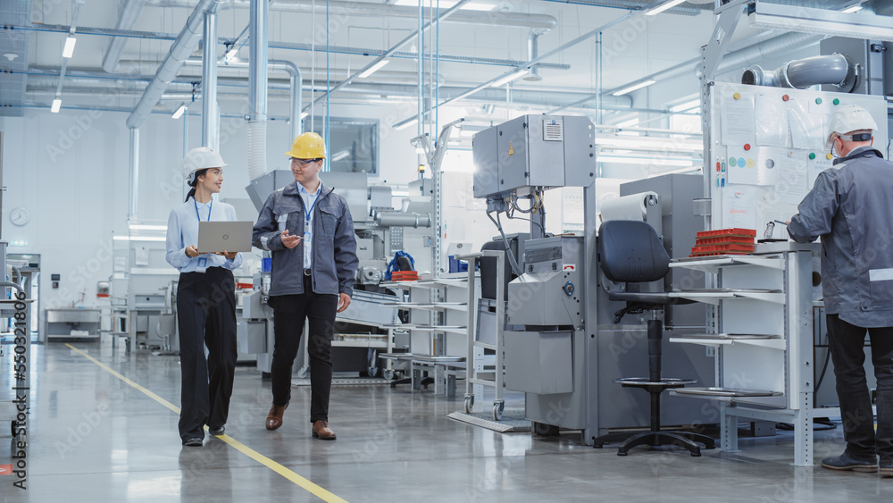 Leinwandbilder wide shot: two heavy industry employees in hard hats discussing job assignments at the factory, usin