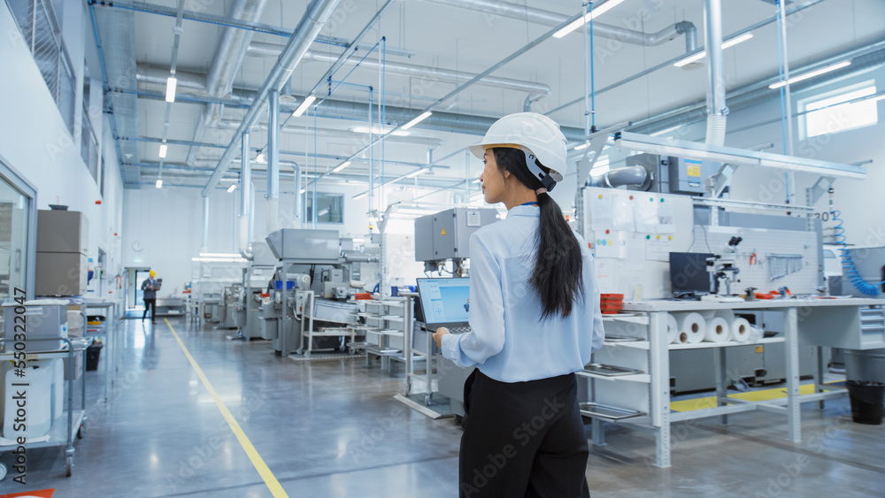 Poster research and development specialist in a factory facility, holding laptop computer and walking in he