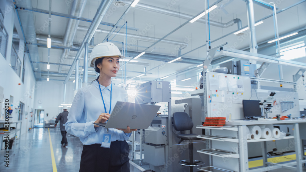 Fototapete Portrait of an Asian Female Engineer in Hard Hat Walking and Using Laptop Computer at Electronic Manufacturing Factory. Technician Working on Daily Tasks and Research and Development Data.
