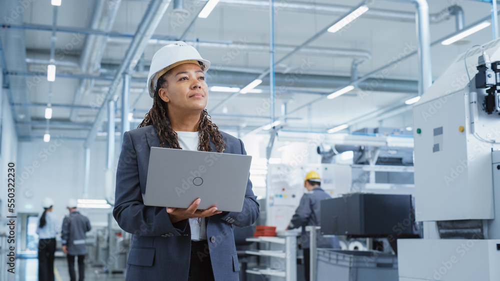 Poster Portrait of a Black Female Engineer in Hard Hat Standing and Using Laptop Computer at Electronic Manufacturing Factory. Technician Thinking About Daily Tasks and Working on Project Pipeline.