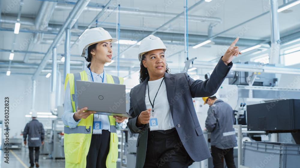 Poster portrait of two female employees in hard hats at factory. discussing job assignments at industrial m