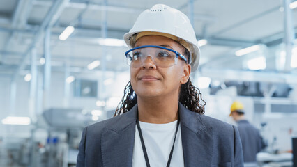 Close Up Portrait of a Happy and Smiling Middle Aged African Female Engineer in White Hard Hat Standing at Electronics Manufacturing Factory. Black Heavy Industry Specialist Supervising Work.