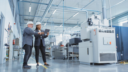 Portrait of Two Heavy Industry Employees in Hard Hats at Factory. Checking and Discussing Industrial Facility, Using Tablet Computer. African American Engineer and Middle Aged Technician at Work.