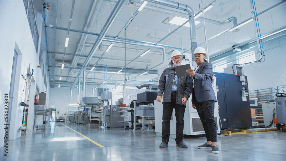 Poster portrait of two heavy industry employees in hard hats at factory. checking and discussing industrial