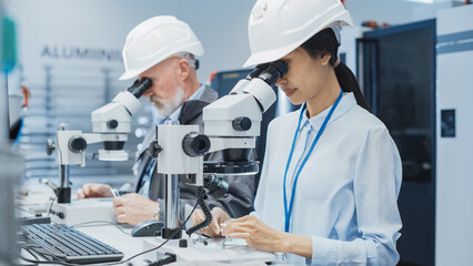 Modern Technology Concept: Two Scientists Examining Small Scale Industrial Equipment Parts Through a Microscope. Technicians Testing New Factory Components for Quality.