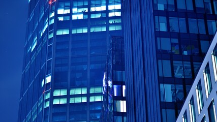 Plakat Pattern of office buildings windows illuminated at night. Glass architecture ,corporate building at night - business concept. Blue graphic filter.