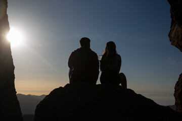 silhouette of a young couple sitting on a rock looking at the sunset