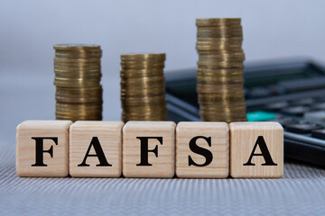 FAFSA - acronym on wooden cubes on the background of coins and calculator