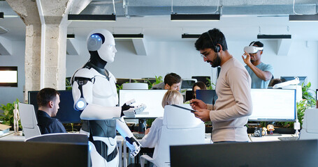 Indian man speaking to robot in office. Male developer checking work and moves of cyborg. Coworking...