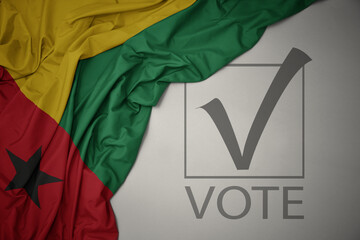 waving colorful national flag of guinea bissau on a gray background with text vote. 3D illustration