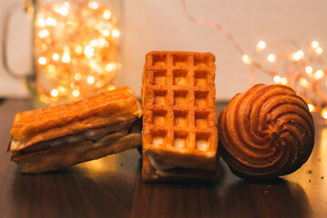 Belgian waffles and Christmas lights. Delicious cakes and waffles, close-up. Sweets for the holidays. Christmas mood. Food background. Dessert