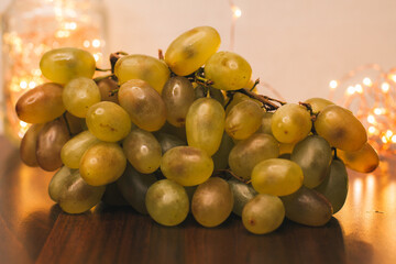Green grapes and Christmas lights from the market. Fresh fruit from the local market. Fruits for the holidays. Ripe grapes, close-up. Healthy diet food