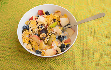 breakfast bowl with cereal and fresh fruits on woven yellow placemat