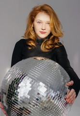 A beautiful young girl model with red hair holds a disco ball. It shimmers in the sun
