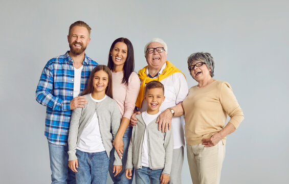 Portrait of happy smiling Caucasian large family consisting of three generations. Young couple, grandmother, grandfather and little brother and sister smiling at camera against background of gray wall