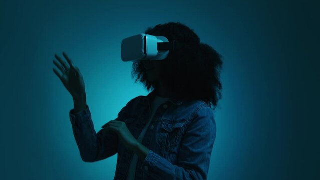 Portrait of a woman watching VR goggles in dark neon-colored room. Brunette, African American girl testing technology program against bluish neon background. High quality 4k footage