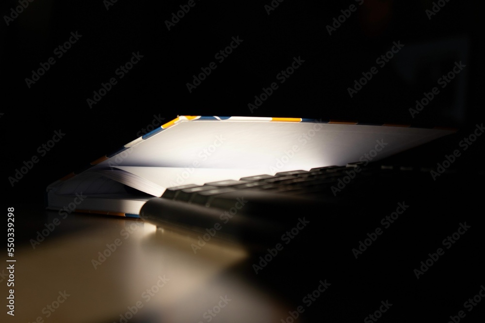 Poster closeup shot a notebook and computer keyboard on a dark background