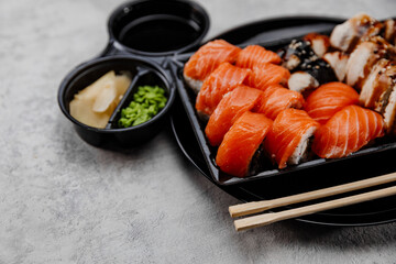 A set of four types of sushi in a black box with Vossabi sauce and ginger on a gray background.Close-up