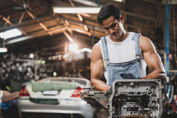 Handsome young male mechanic and car repair service man using various tools to repair engine motor wearing overalls and hand gloves in modern garage and maintenance workshop during daytime