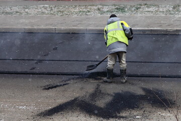 Road worker digs new asphalt with a shovel, asphalting by the pit method, road repair construction on city street at autumn. Top view