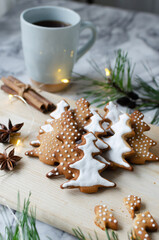 Festive cookies decorated with white icing on a wooden cutting board with a hot drink in a blue cup on a marble background with lights. Homemade ginger and cinnamon Christmas cookies. 