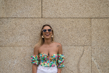 Young beautiful blonde woman with sunglasses leaning against a brown wall in different postures and...
