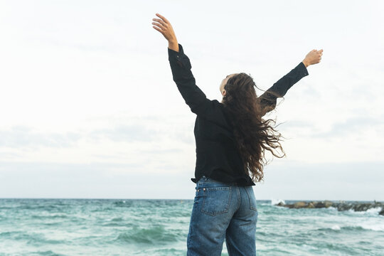 Anonymous content woman with arms stretched on sandy seashore