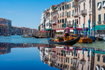 Fototapeta na wymiar Gondolas on the Grand Canal of Venice on a summer day, reflections of vintage Venetian houses while traveling through the canals of Venice in Italy in summer. Italian architecture and landmarks