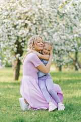 Obraz premium Mom and little daughter walk through the blooming spring garden and hug