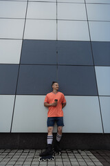 Wide angle view of smiling roller skater holding coffee to go near building outdoors.