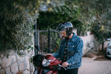 A young man in a helmet starts a motorcycle near the gate of the house.