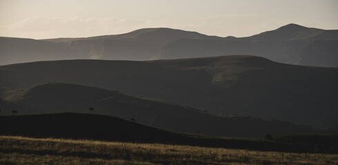 Panorama of mountain ranges with hills and vegetation on them, at evening sunset lighting