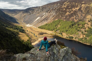 Woman sitting on the edge of a cliff, enjoying the landscape. Glendalough, Wicklow, Ireland.